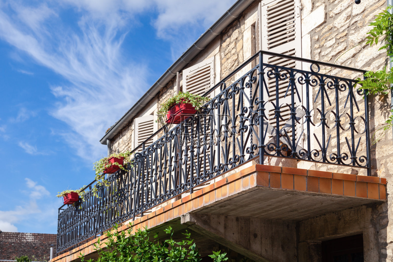 舒适的复古法式阳台，黑色金属栏杆，花盆里的花，窗户上的百叶窗对着蓝天，云彩。底部视图。欧洲意大利概念旅游，古色古香的街道，古老的建筑照片摄影图片