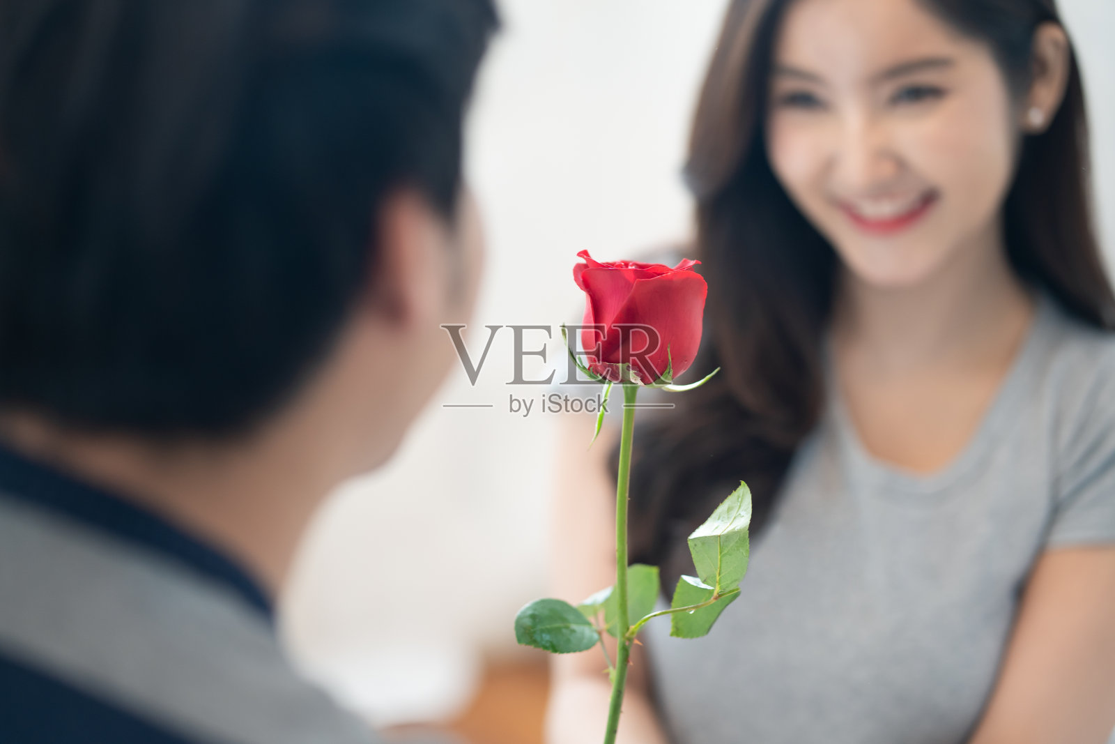 亚洲年轻人给红玫瑰花漂亮的女人。女孩收到可爱的情人节礼物感觉爱和害羞的微笑在脸上。关注美丽的花朵。男孩和女孩，夫妻关系概念照片摄影图片