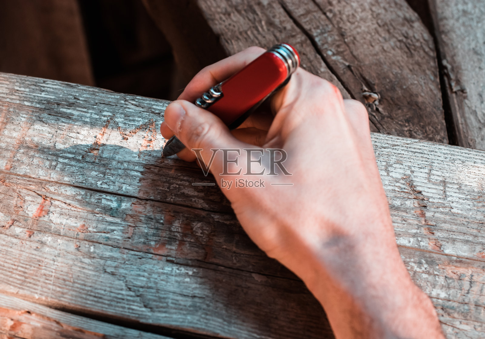 手里拿着一把红色的多功能小刀，在木梁上刻着一个签名。故意破坏公物的行为照片摄影图片