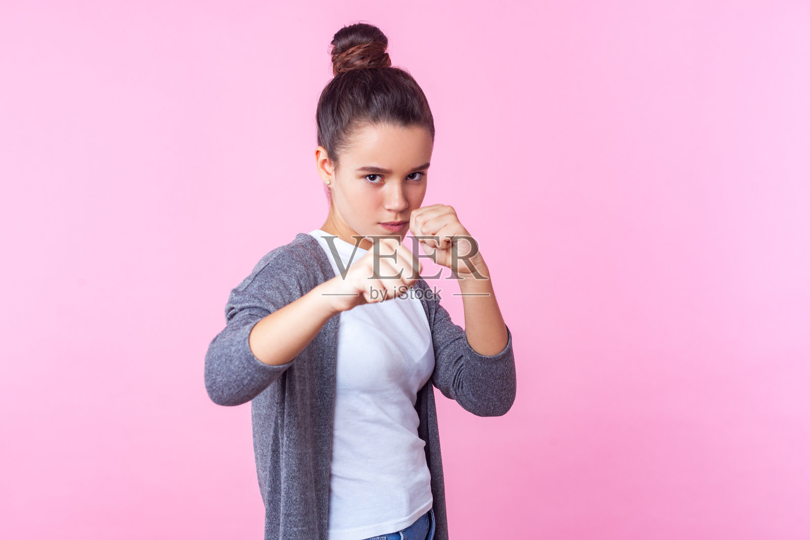 肖像勇敢的少女站在防卫姿势举起拳头，准备出拳。工作室拍摄，粉色背景照片摄影图片
