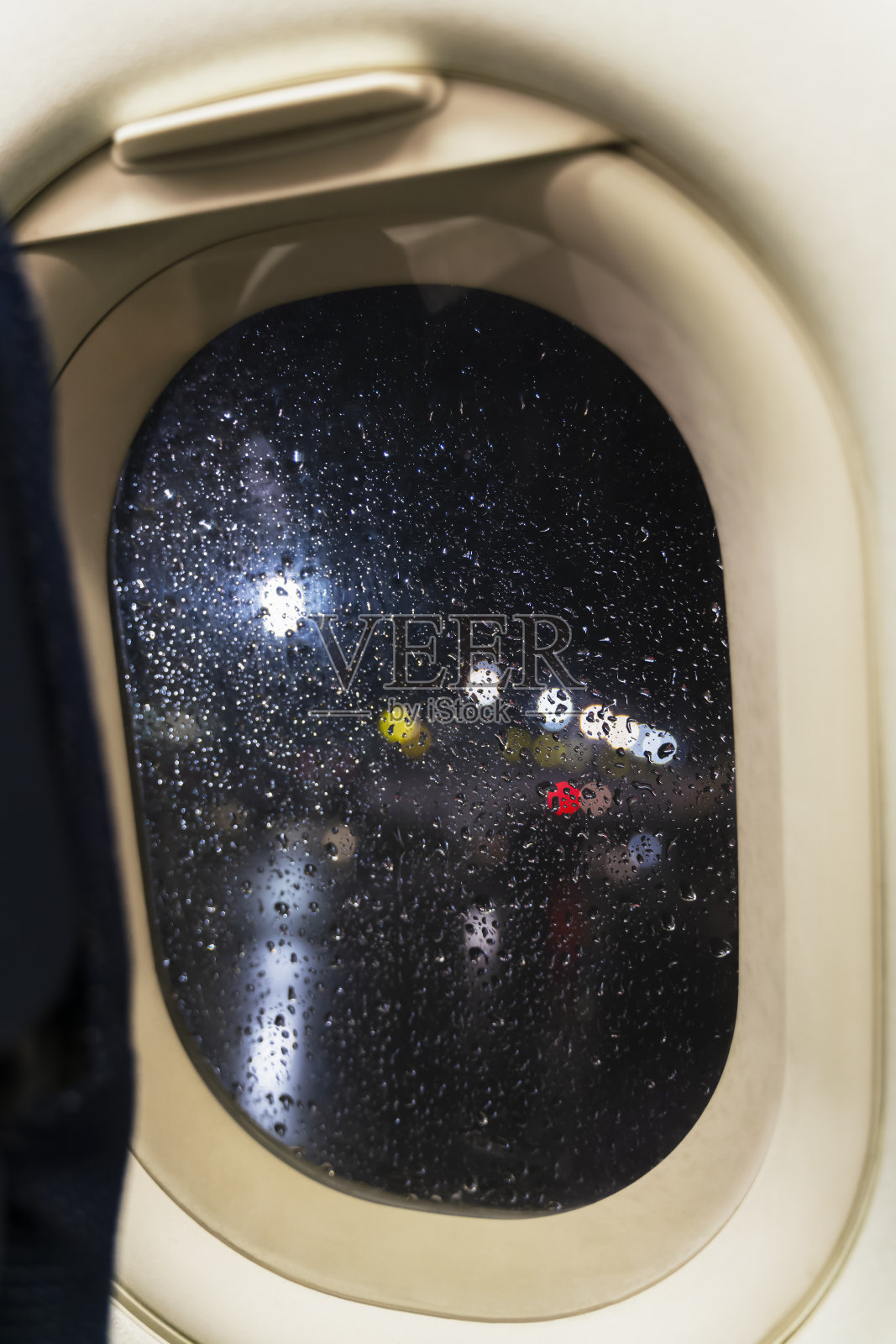 夜景从飞机客舱窗口的多色机场灯。由于恶劣的下雨天气，雨的散布在视口。带你去热带国家的飞机。旅行的概念。照片摄影图片