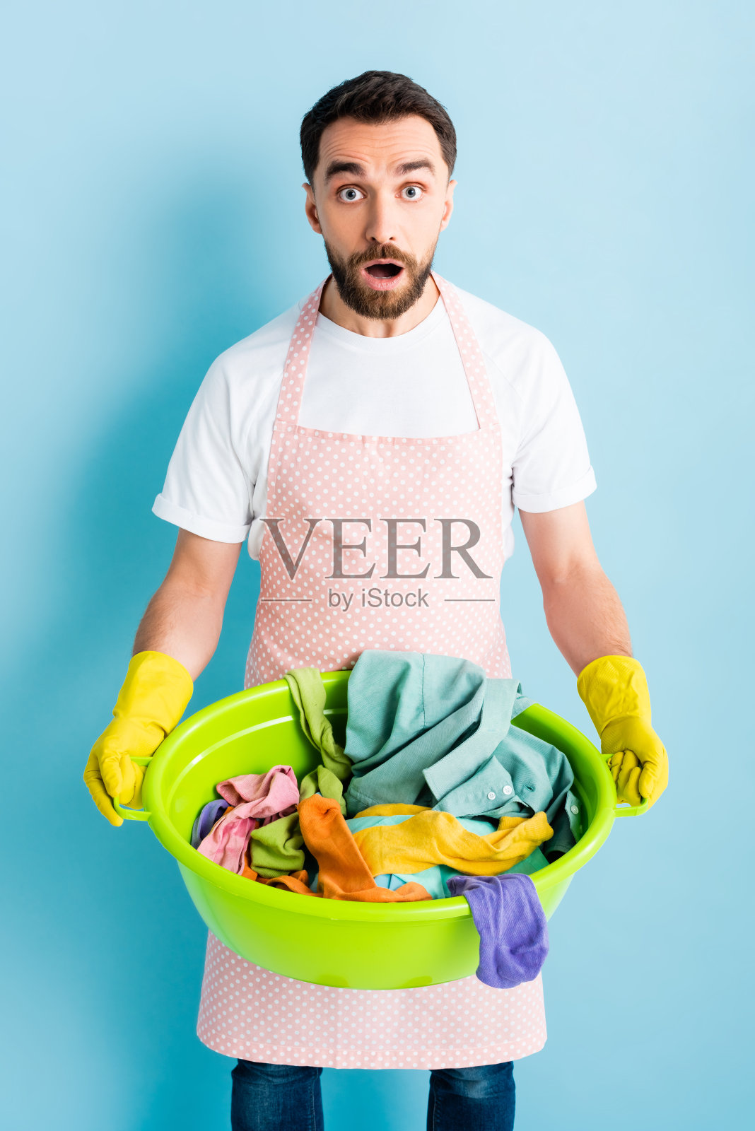 震惊的男人在橡胶手套拿着洗碗脏衣服在蓝色照片摄影图片