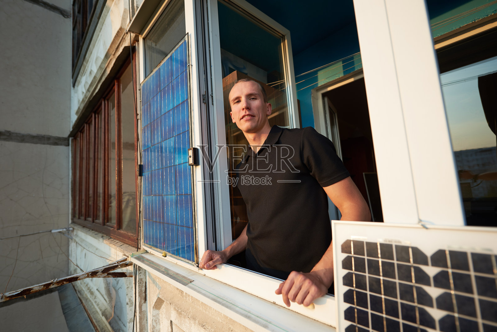 男在多层建筑的阳台上装有太阳能电池板，以城市为背景照片摄影图片