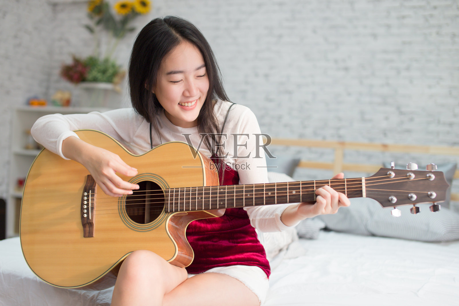 可爱和快乐的微笑亚洲女孩在卧室弹吉他照片摄影图片