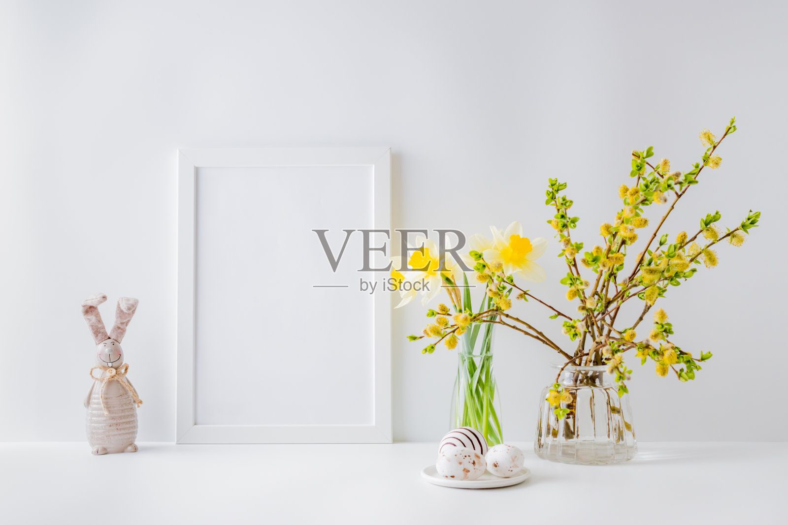 家庭内部与复活节装饰。模型与白色框架和柳树枝在玻璃花瓶在一个光的背景照片摄影图片