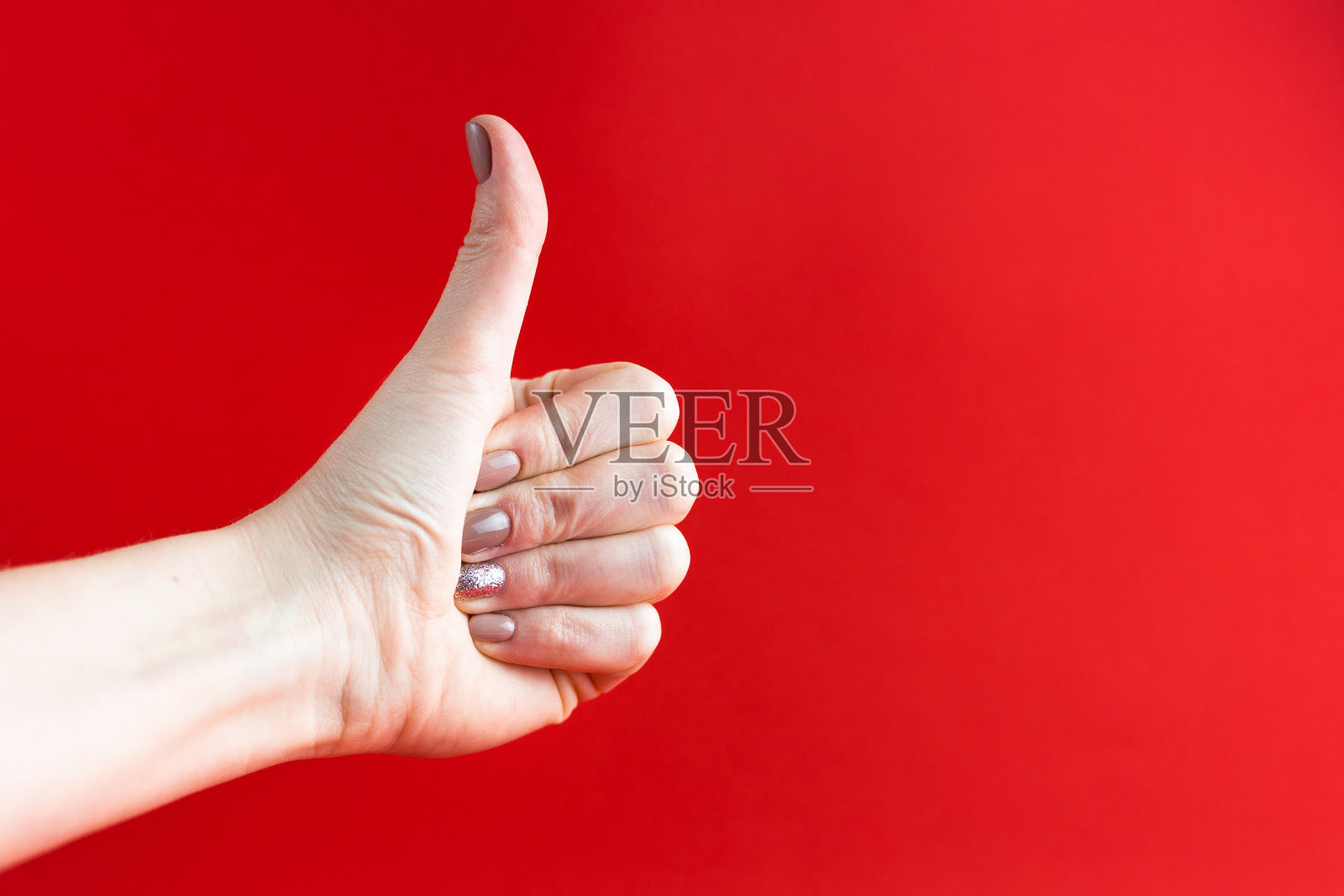女人的手用米色修指甲孤立在红色背景上，拇指向上翘起，像概念一样照片摄影图片