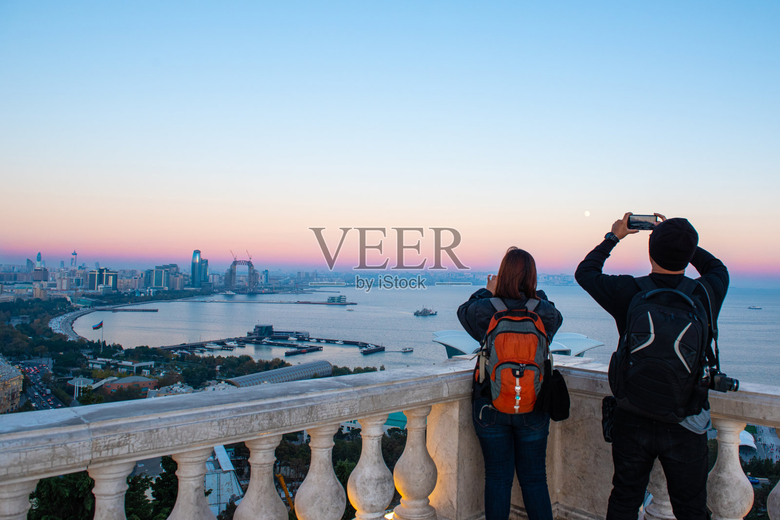 夫妇旅行者使用智能手机和相机拍照的观点巴库里海和巴库天空景观在日落在布库视点与复制空间。照片摄影图片
