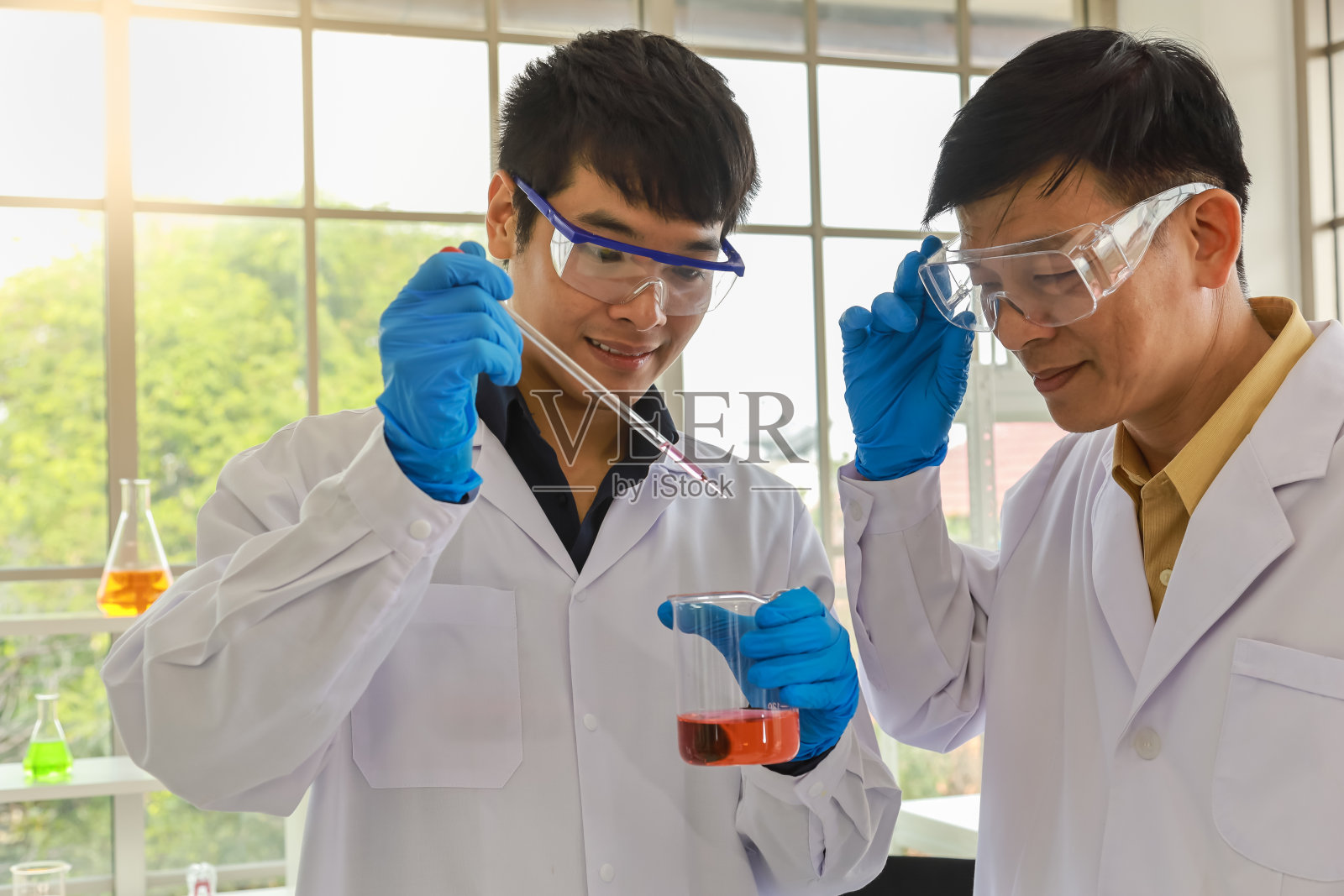 亚洲专业资深博士科学家的近距离教学和指导亚洲青年科学家使用移液管在工作实验室进行测试和研究。照片摄影图片