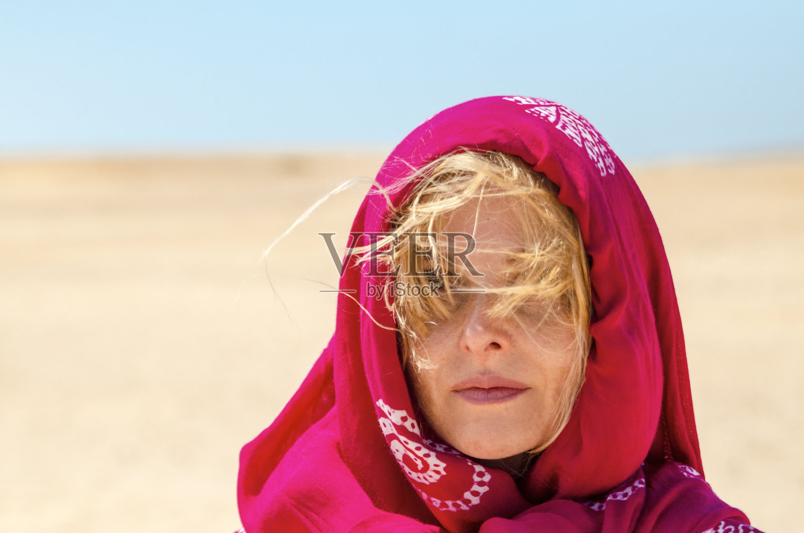 头上戴着红围巾的女人在沙漠的风中放松地行走照片摄影图片