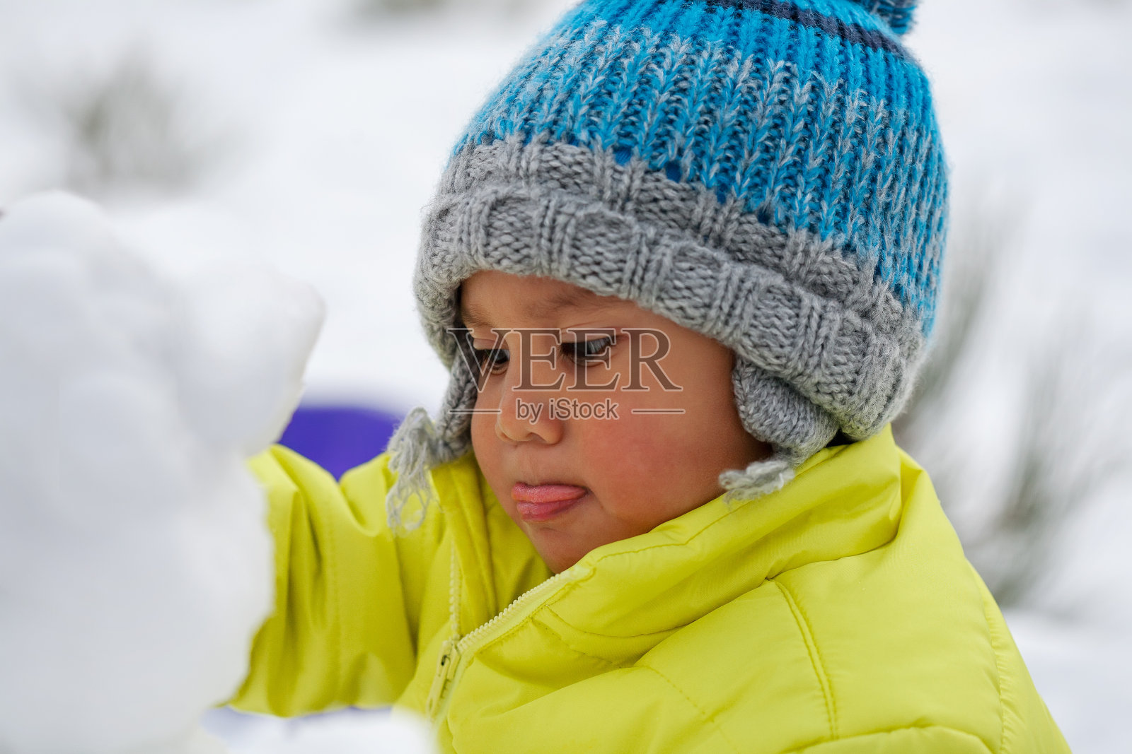 一个孩子在雪地里聚精会神地堆雪人，穿着冬衣。照片摄影图片