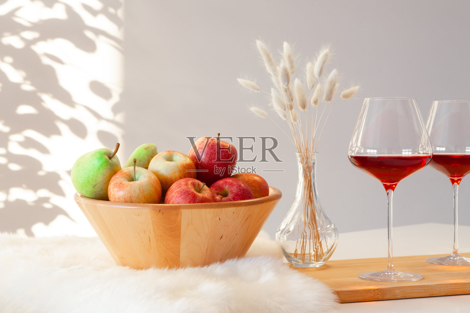 两杯勃艮第红酒，木碗和红绿苹果，装饰花瓶在白色背景的厨房桌子上。Copyspace。放置文字，室内目录，品酒照片摄影图片