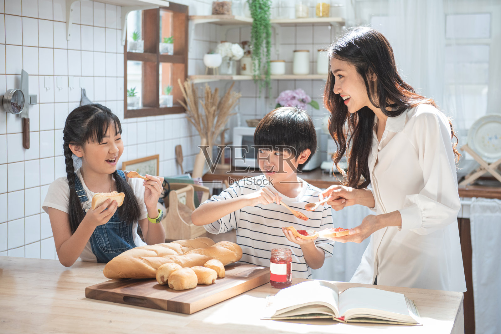 母亲、儿子、女儿和孩子们把草莓山药涂在厨房的面包上。照片摄影图片