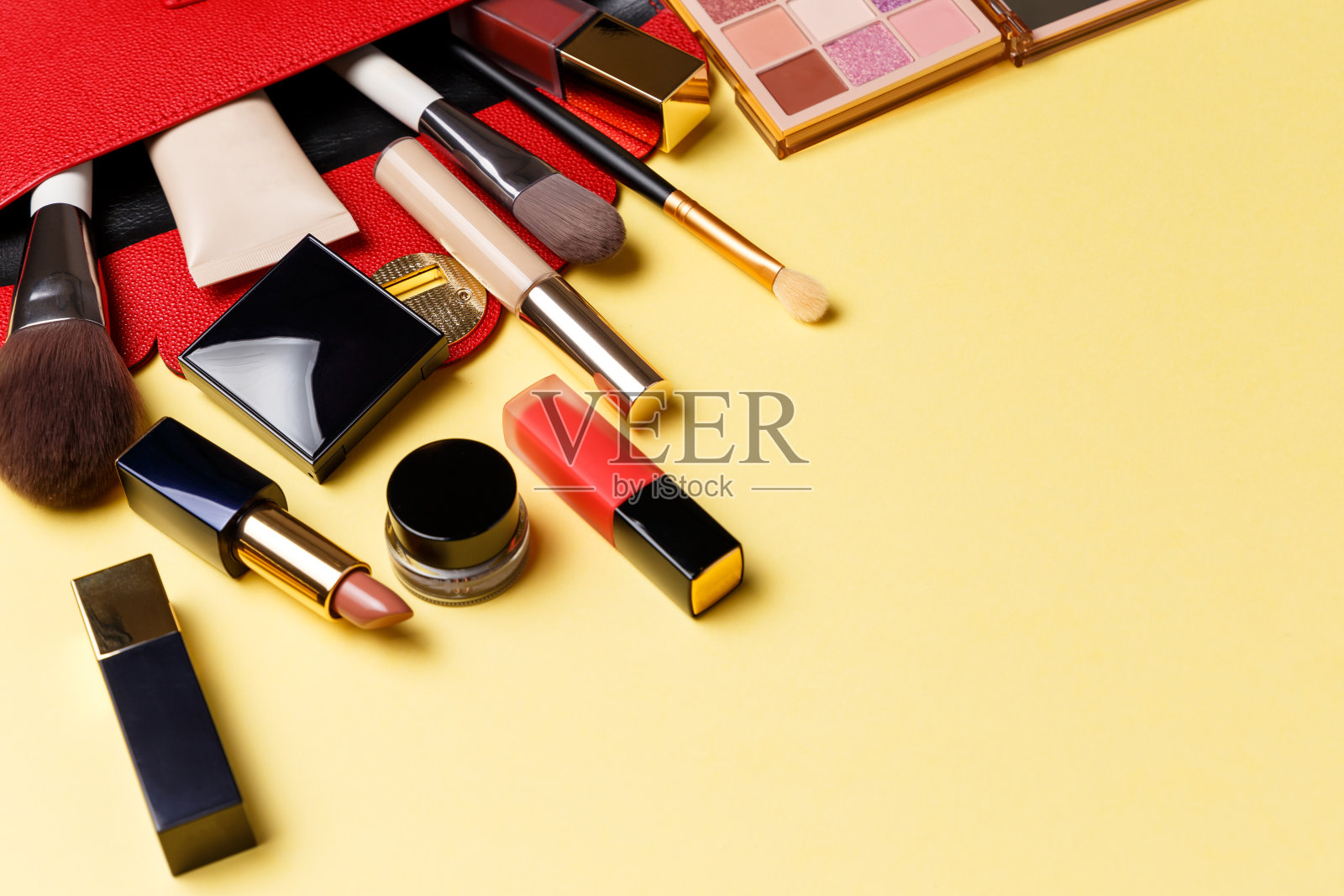 一套专业的精英装饰化妆品化妆上黄色的背景。美丽和时尚的概念。一个红色的化妆包，里面有化妆品:口红、眼影、粉底照片摄影图片