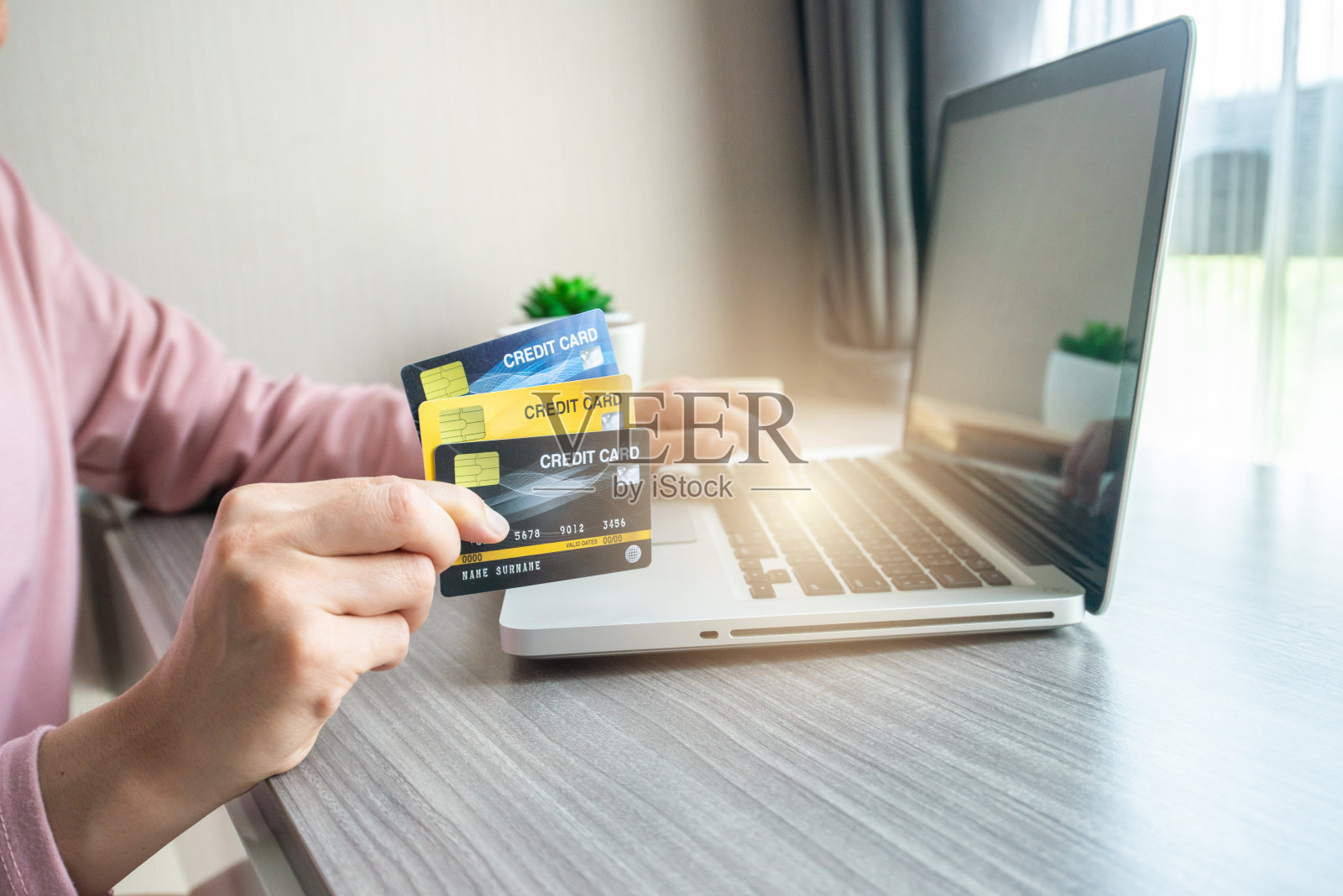 在使用笔记本电脑进行网上购物期间，女性手握信用卡的特写。照片摄影图片