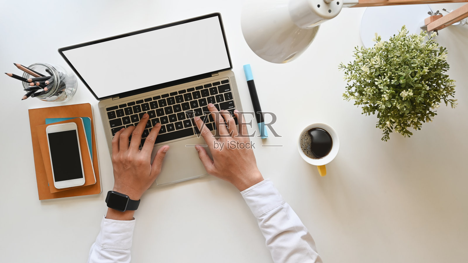 俯视图，商人打字在白色空白屏幕的笔记本电脑在现代的办公桌。包括办公桌上的工作设备。照片摄影图片