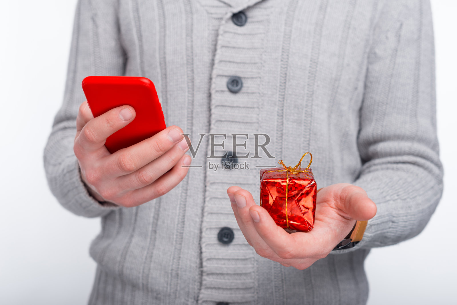在网上买礼物。男人手里拿着他的手机和一份红色的礼物。向你的母亲、妻子和女儿问好。照片摄影图片