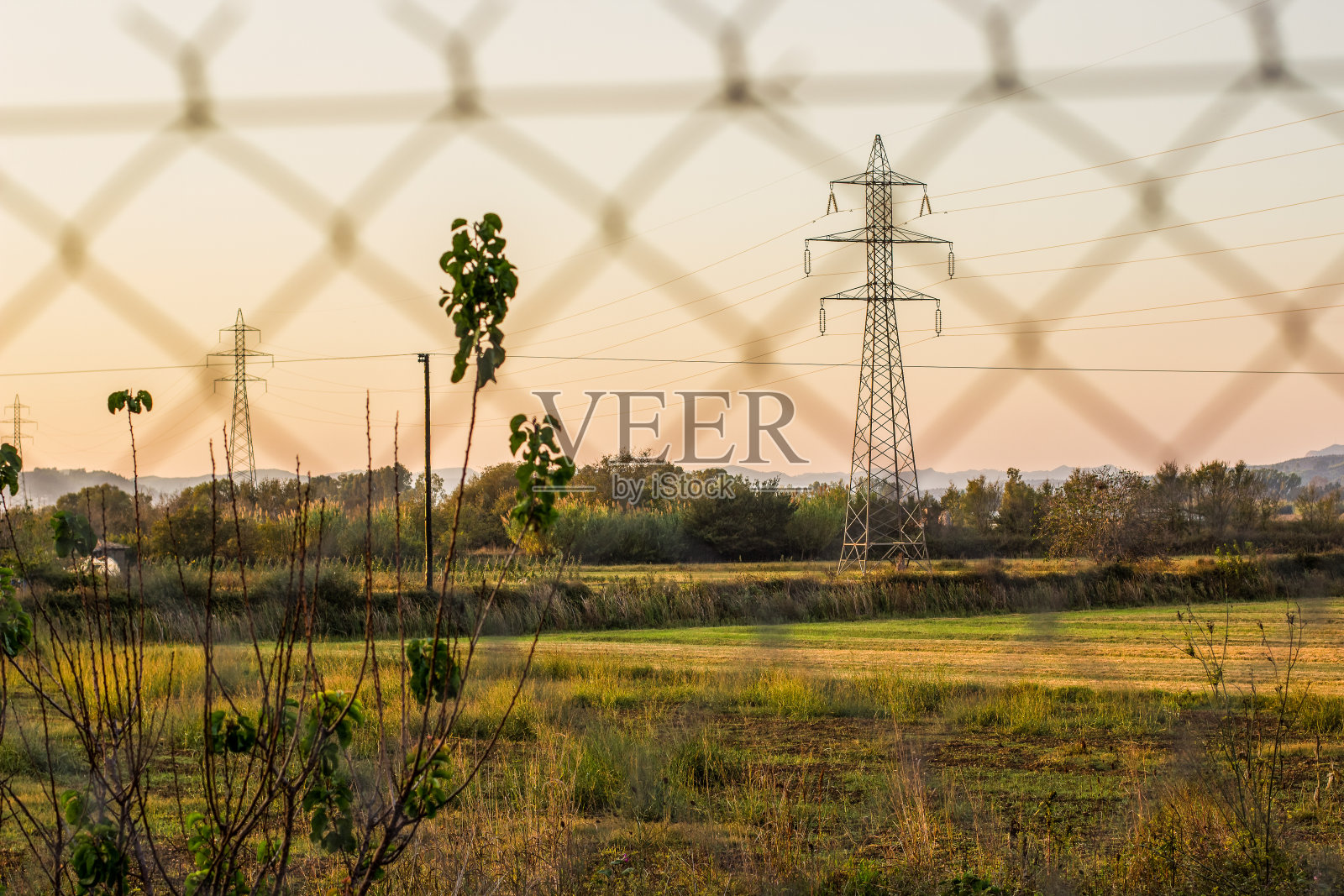 高压电线塔的工业概念射穿了村庄的金属栅格围栏，在黄昏的夕阳中，乡村边的环境山谷里呈现出金色的色彩照片摄影图片