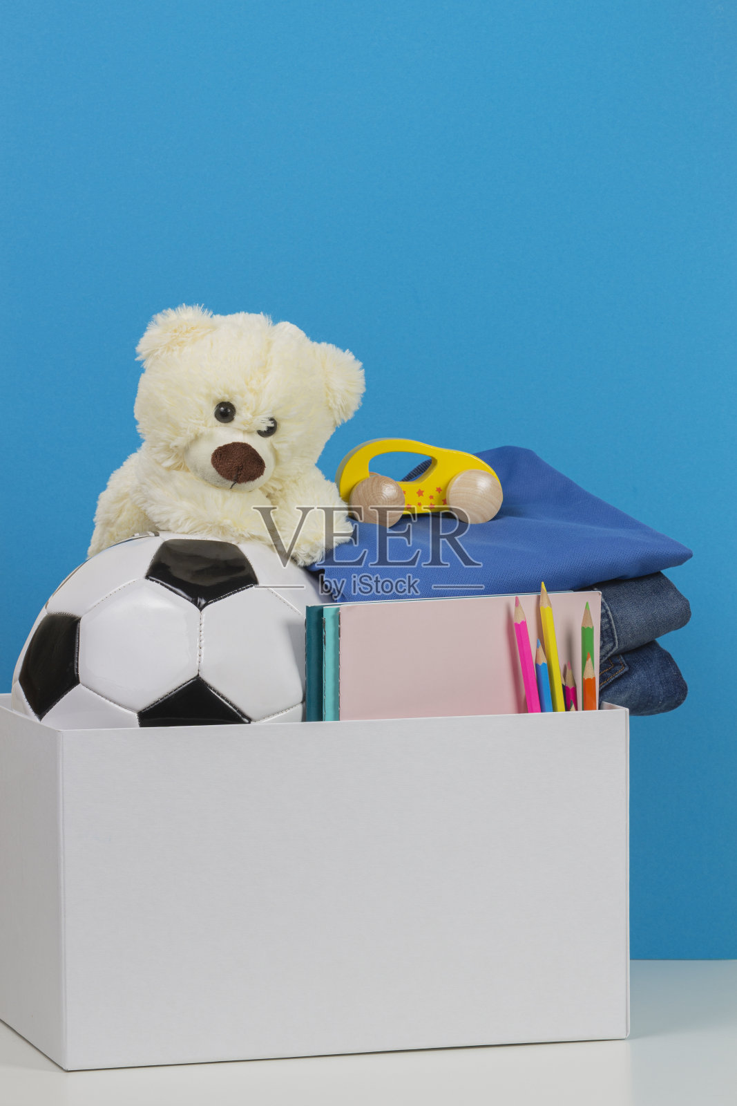 蓝色背景的白色桌子上放着捐赠箱，里面有玩具、书籍、慈善衣物照片摄影图片