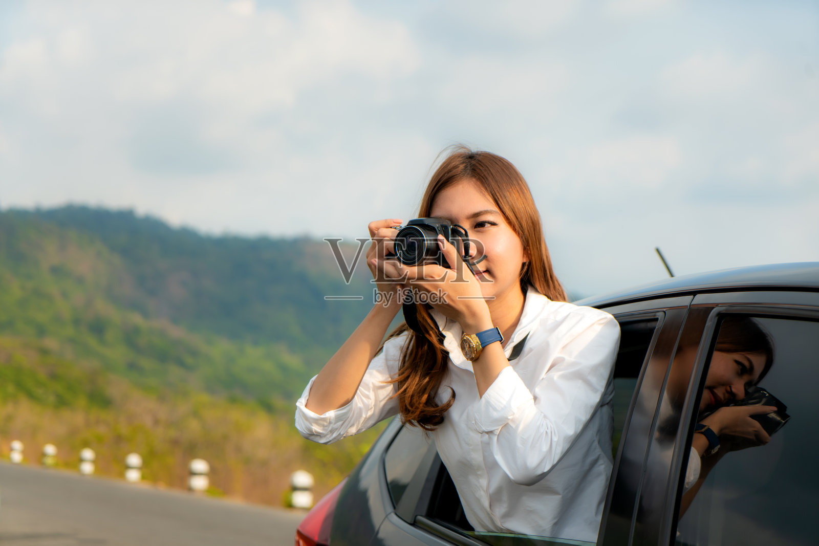 年轻的亚洲女性游客拍照在汽车与相机驾驶公路旅行度假。女乘客向窗外拍照，背景是美丽的湖和山。照片摄影图片