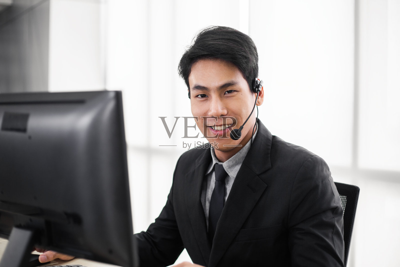 快乐自信微笑的亚洲商务人员在服务台打电话呼叫中心，男性接线员的肖像与耳机，客户服务或技术支持概念照片摄影图片