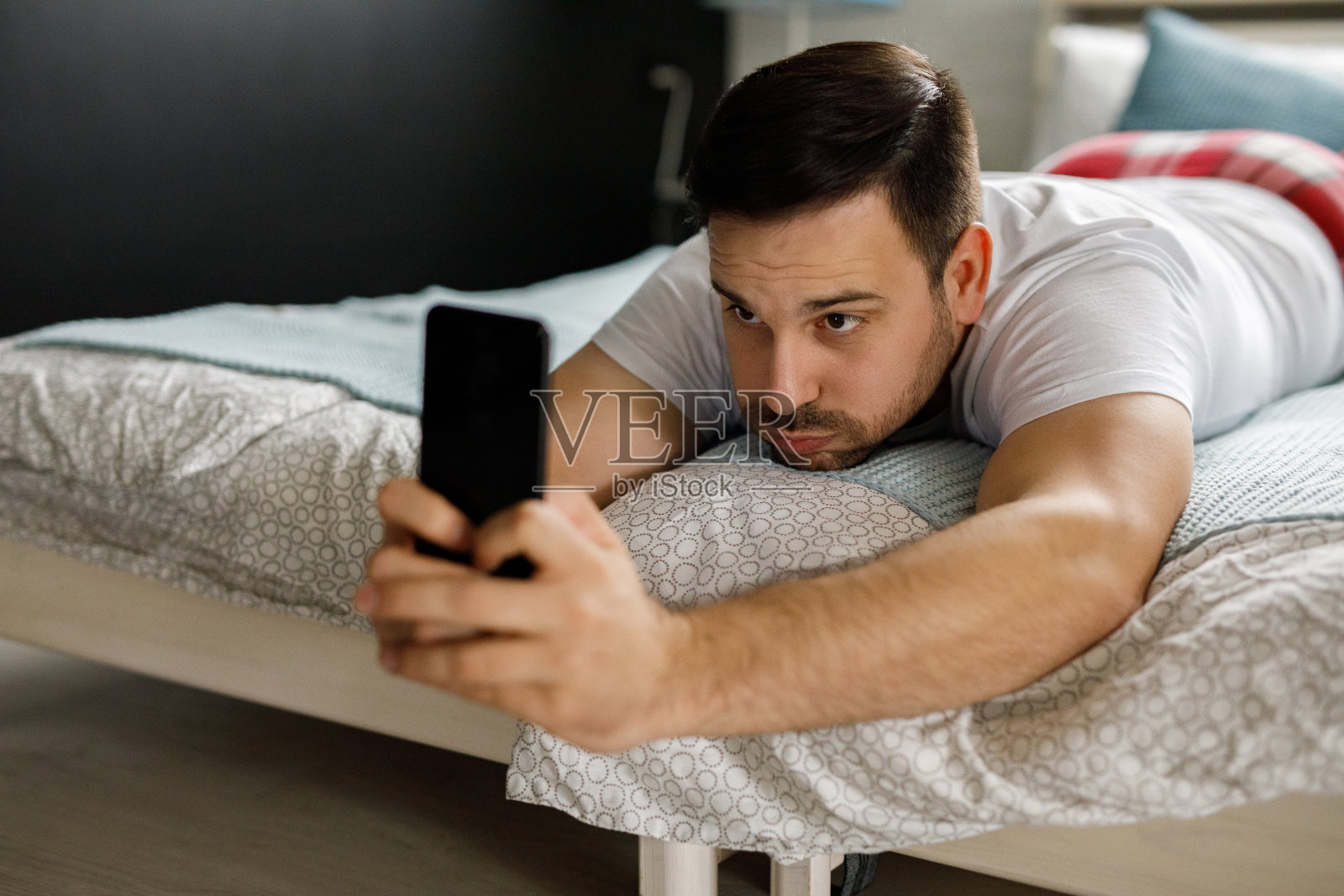 年轻人躺在卧室的床上，用智能手机照片摄影图片