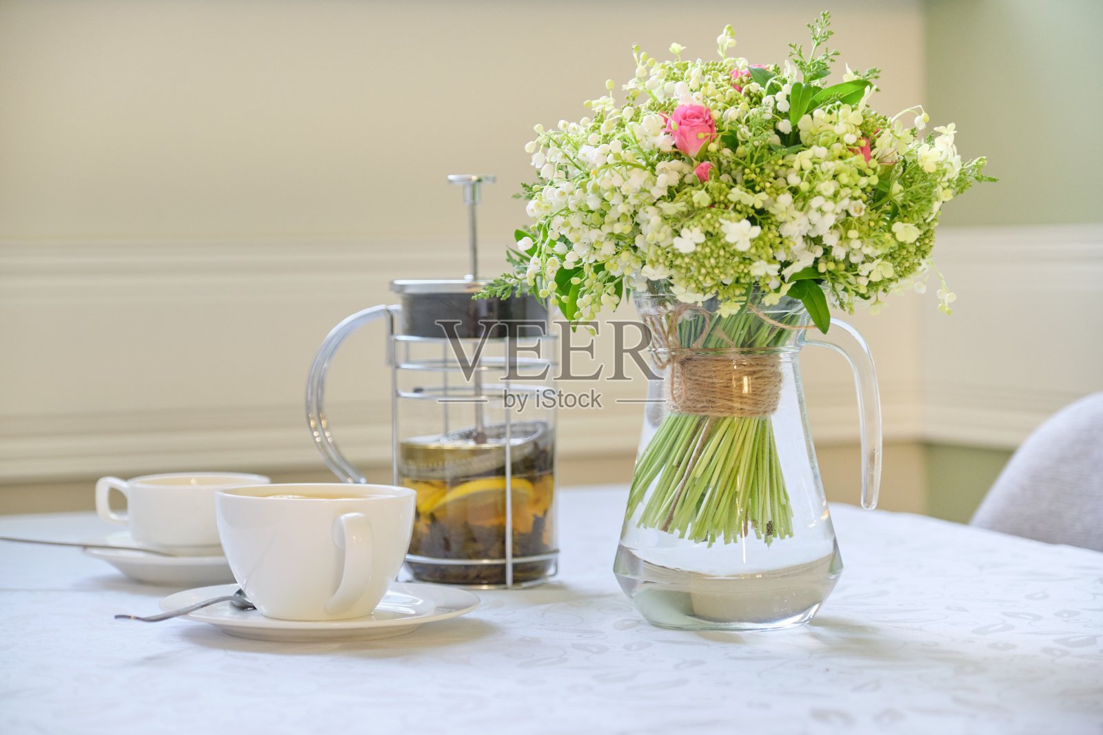 桌上铺着白色桌布，茶壶，茶杯和一束美丽的鲜花照片摄影图片