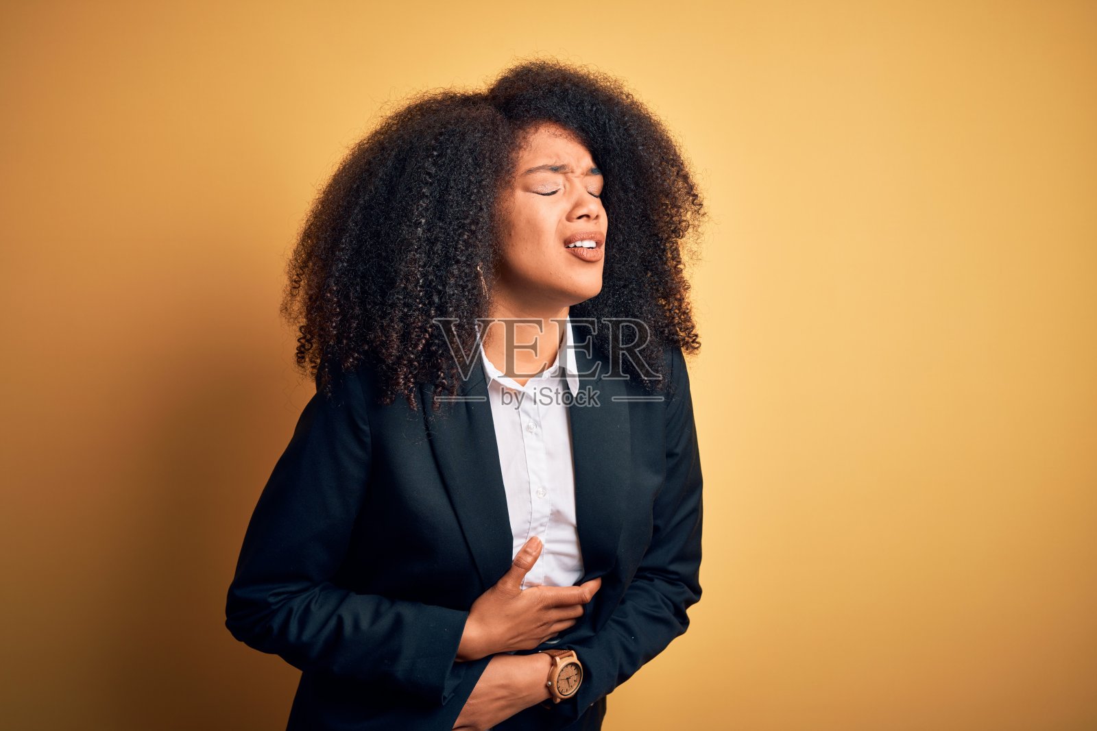 年轻美丽的非洲裔美国商务妇女与非洲式的头发穿着优雅的夹克与手在胃部，因为消化不良，痛苦的疾病感觉不舒服。疼痛的概念。照片摄影图片