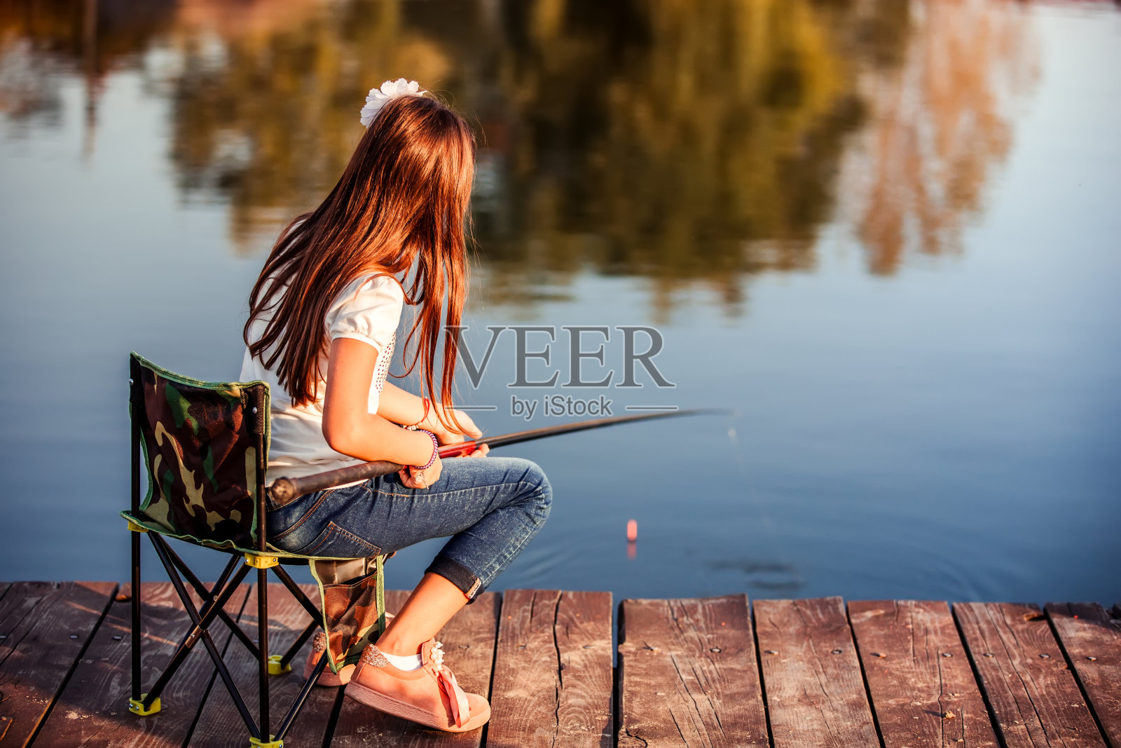 一个白人小女孩拿着钓竿坐在木码头上。照片摄影图片