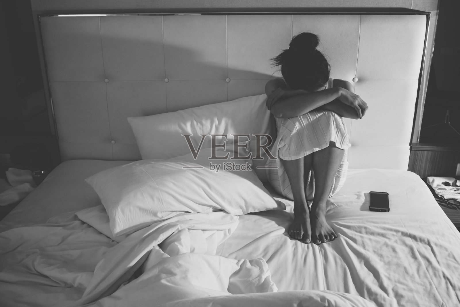 忧郁的女人独自坐在卧室的床上的肖像/黑白色调。照片摄影图片