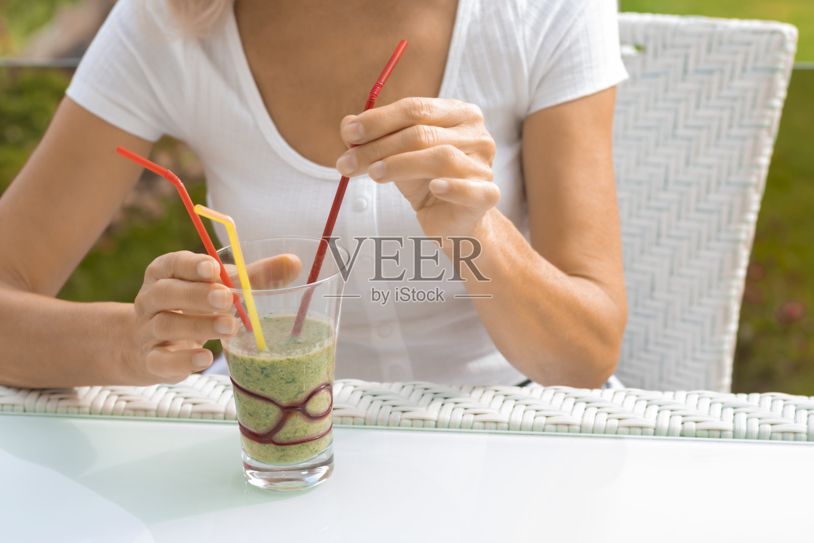 女性的手拿着一杯绿色健康的奶昔鸡尾酒，用吸管。在乡下的房子里吃健康的生蔬菜早餐照片摄影图片