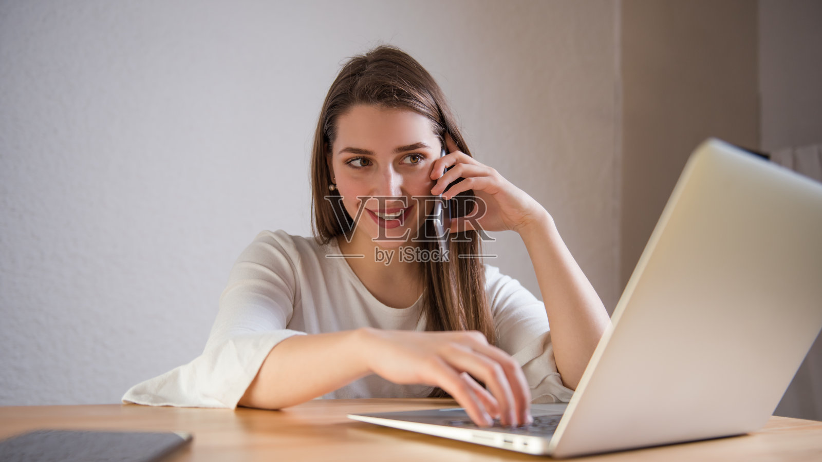 女人在笔记本电脑上打字，在智能手机上讲话照片摄影图片