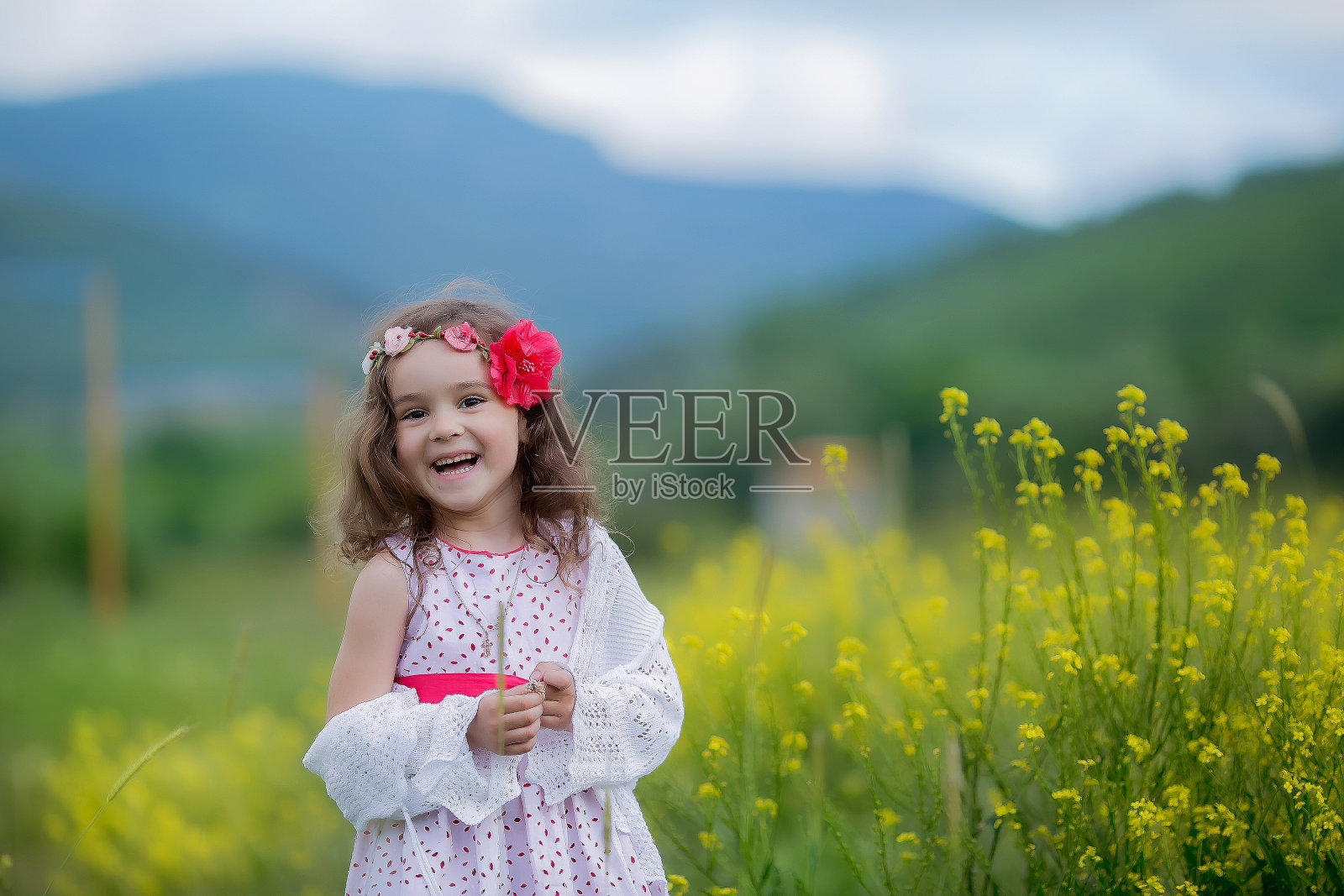 一个孩子的头发上插着一朵花，在风景如画的群山背景下玩耍照片摄影图片