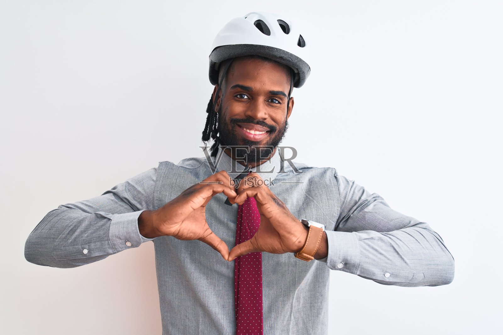 非洲裔美国商人与辫子戴自行车头盔在孤立的白色背景微笑在爱显示心形符号和形状的手。浪漫的概念。照片摄影图片