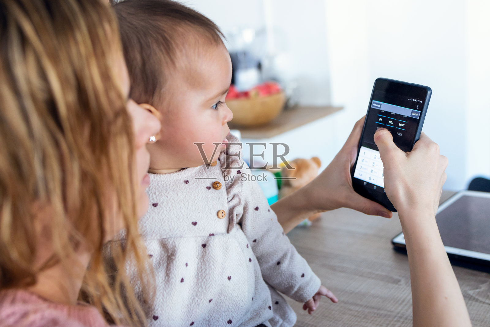 一个年轻的女人在用她的手机，而她的女儿在家里看手机。照片摄影图片