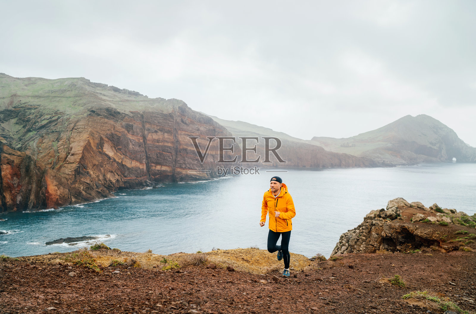 一名身穿橙色防水夹克、紧身衣和跑鞋的跑步者在葡萄牙马德拉岛最东端的蓬塔·德·圣LourenÃ§o半岛的大西洋海湾山脉慢跑照片摄影图片