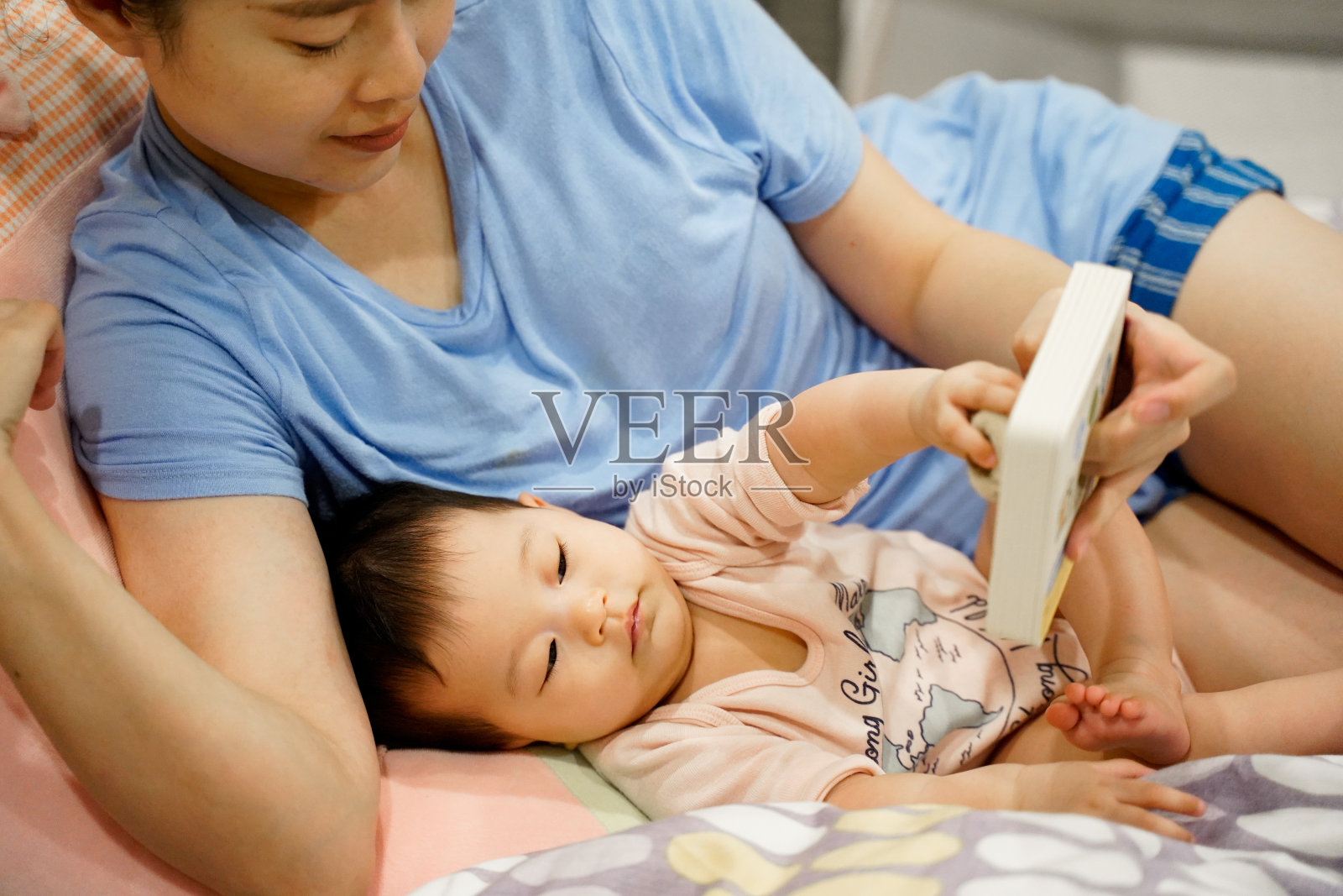 妈妈和小女孩在床上看书准备睡觉，小宝贝躺在妈妈的手里拥抱着。照片摄影图片