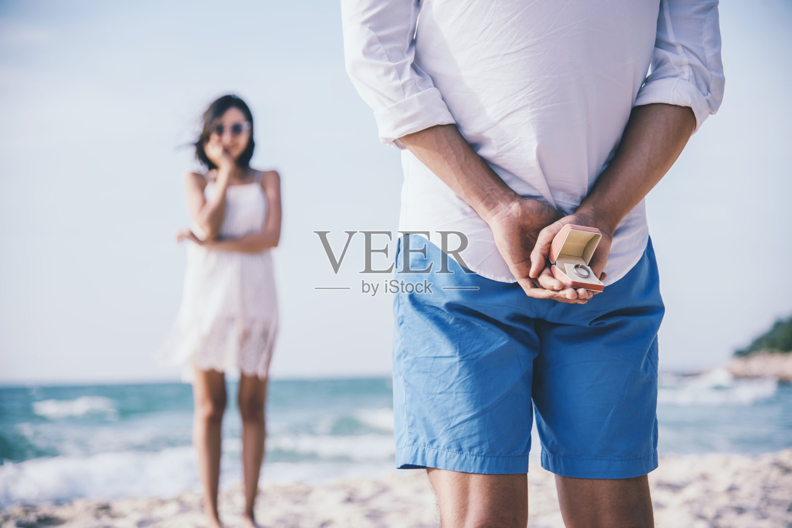 一个男人在沙滩上向他的女朋友求婚，把戒指藏在后面。爱情和婚姻观念。照片摄影图片