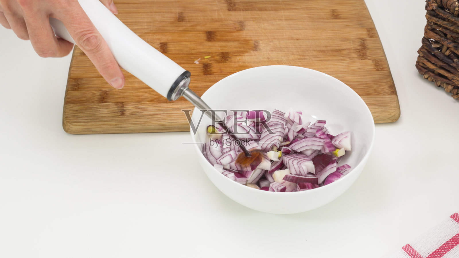 用碗把腌制好的红洋葱切成小块放在白色餐桌上。女人加酱油照片摄影图片