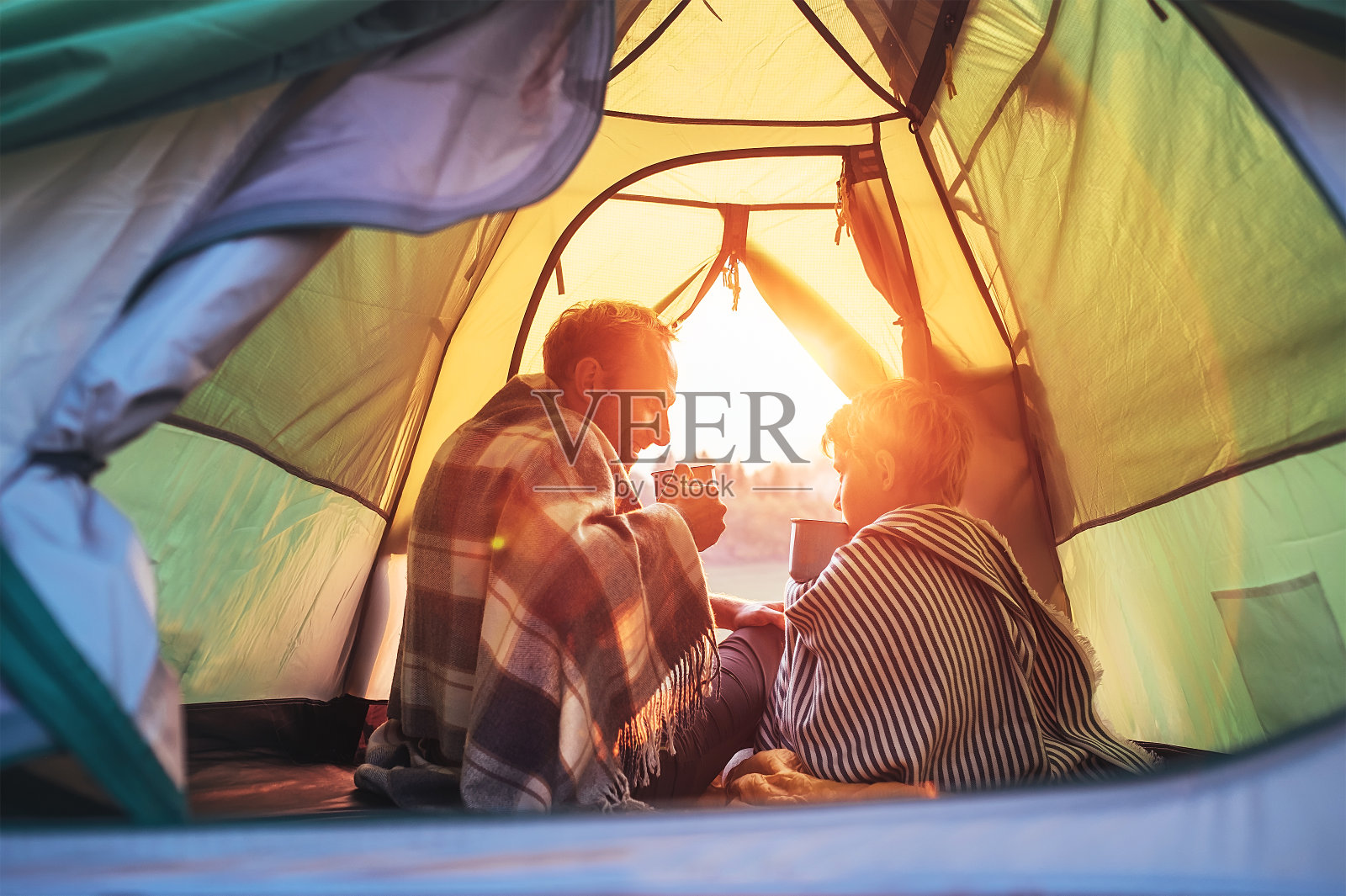 父子俩一起坐在帐篷里喝着热茶。与孩子和活跃的人一起旅行的概念形象。照片摄影图片