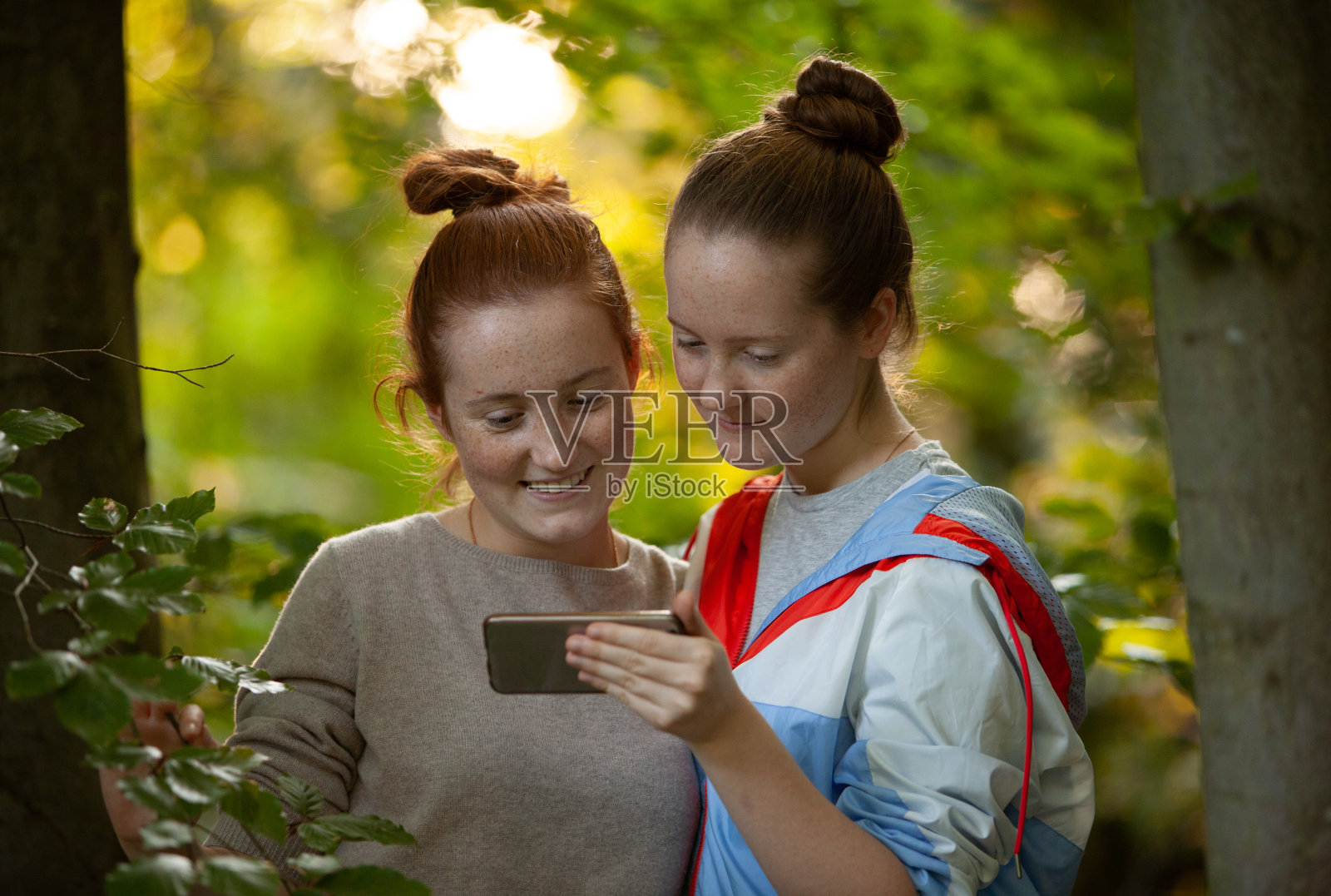 两个女孩在森林里，用智能手机查看社交媒体照片摄影图片