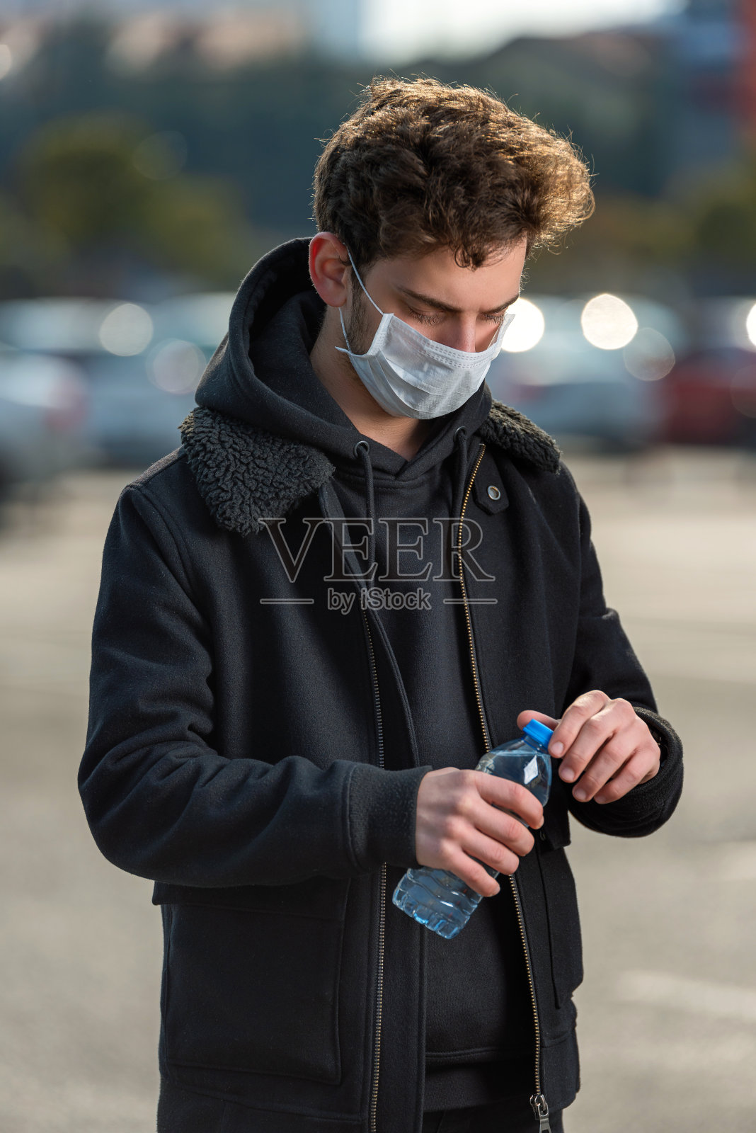 一名戴医用口罩的年轻人正在用塑料瓶喝水，以预防冠状病毒照片摄影图片