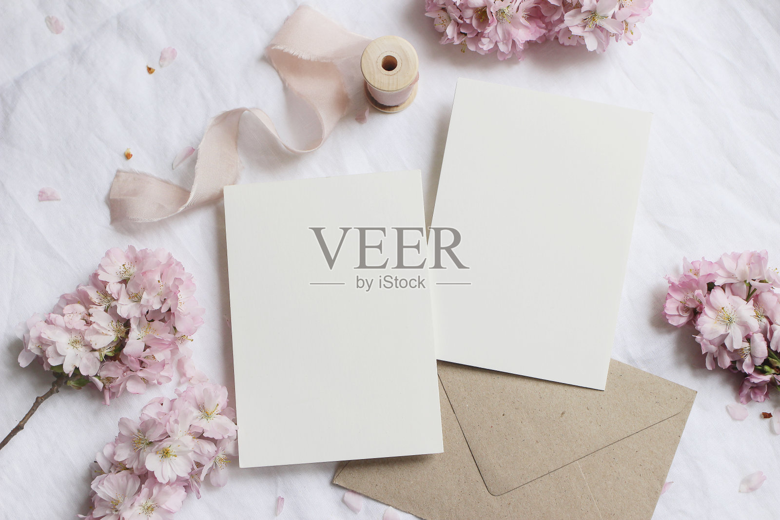 婚礼文具模型场景。空白贺卡，信封在亚麻桌布的背景与粉红色樱花树枝和丝带。女性静物构图。平坦的躺,俯视图照片摄影图片