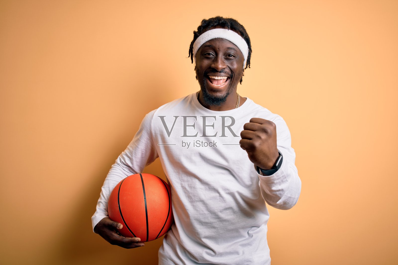 年轻的非洲裔美国运动员在做运动，拿着篮球在黄色的背景下尖叫，庆祝胜利和成功非常兴奋，欢呼的情绪照片摄影图片