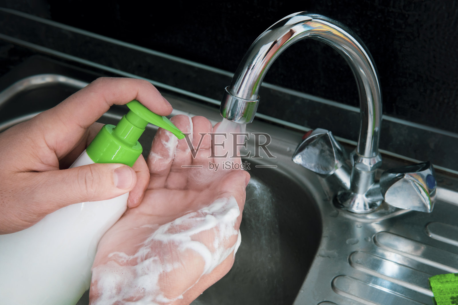 男人用瓶子里的洗手液洗手。COVID-19卫生的概念。用肥皂在水龙头下用水洗手，防止新型冠状病毒感染。杀菌、卫生、保健理念。照片摄影图片