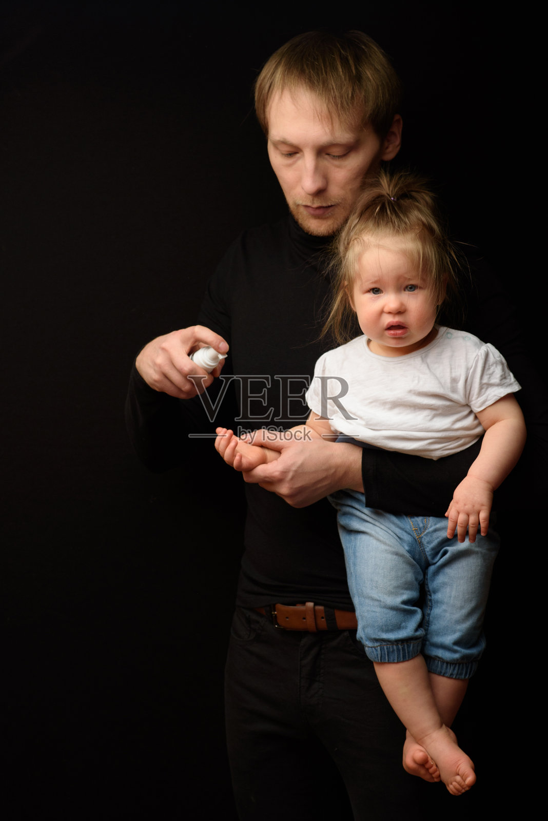 一位父亲用杀菌剂给小女儿消毒双手。新冠肺炎疫情期间保护儿童的理念照片摄影图片