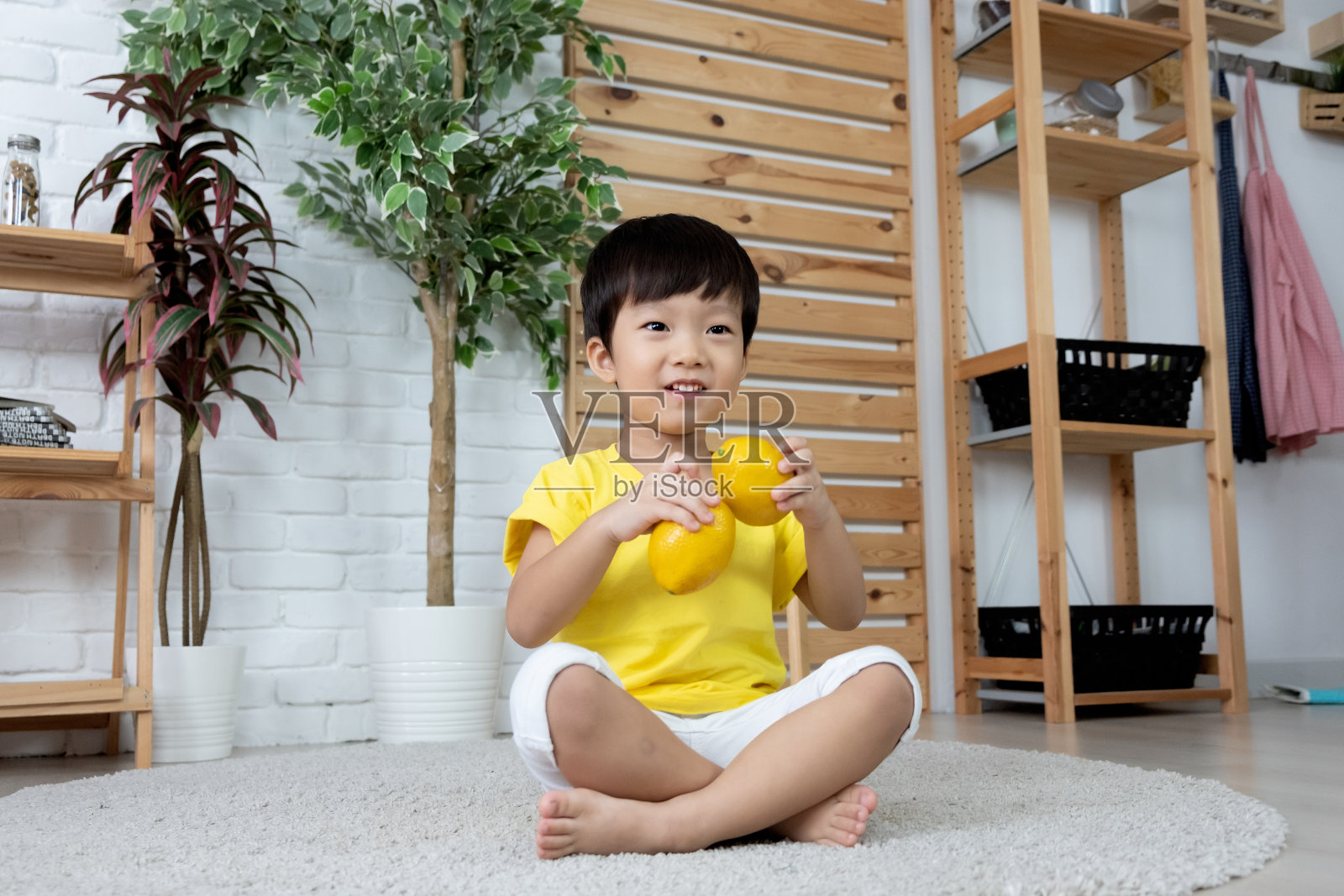 一个亚洲幼童坐在厨房里玩橘子照片摄影图片