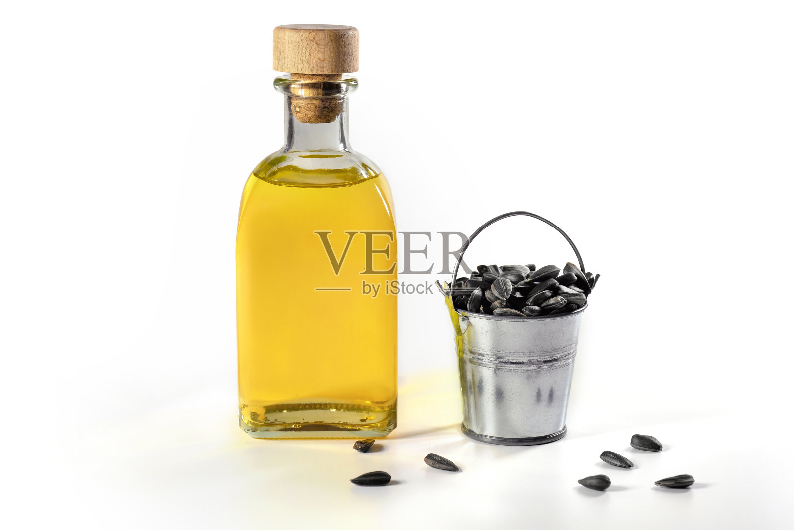一瓶葵花籽油和一桶种子在白色的背景。照片摄影图片