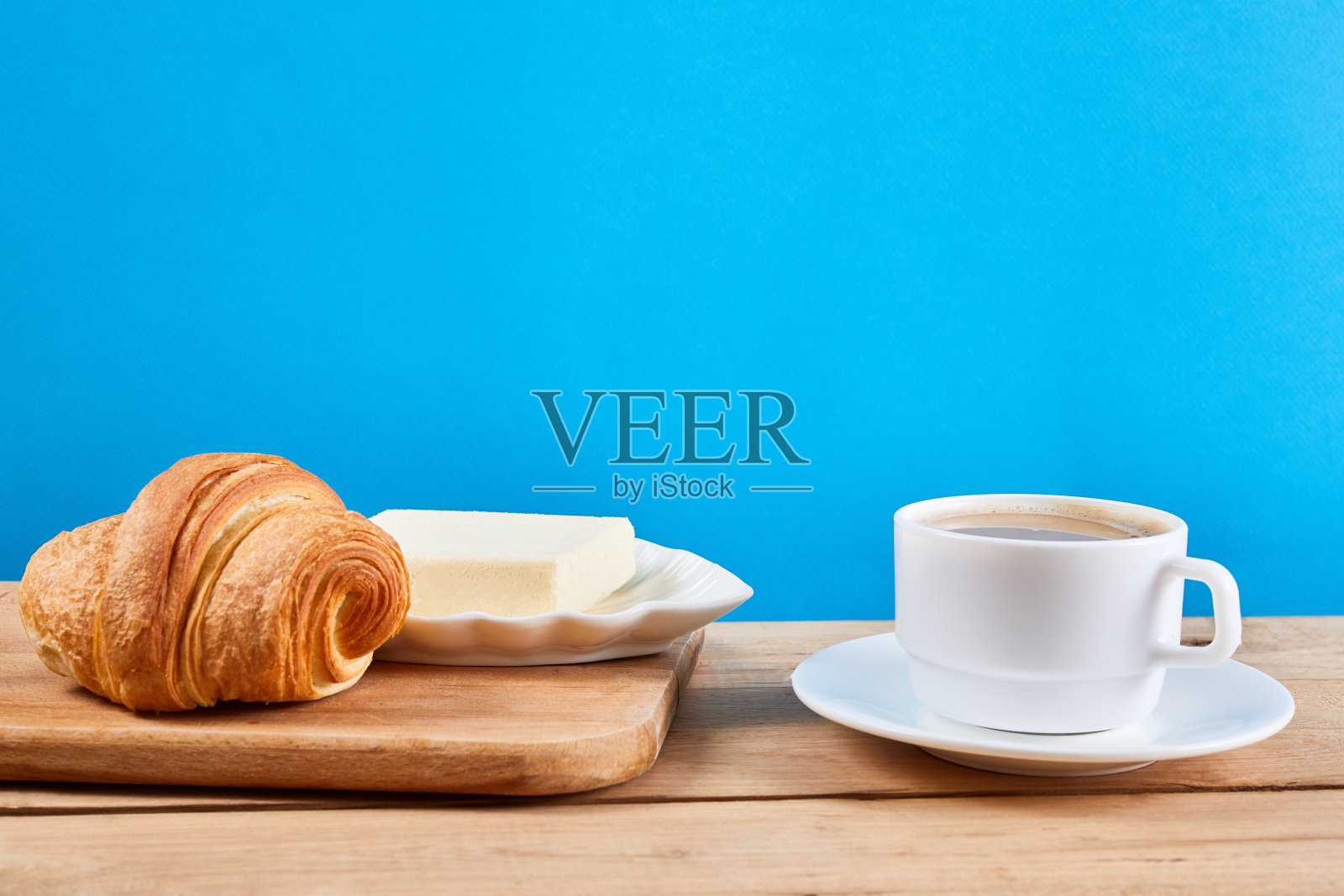 咖啡早餐，牛角面包，黄油和一杯黑咖啡放在橡木木桌上。照片摄影图片