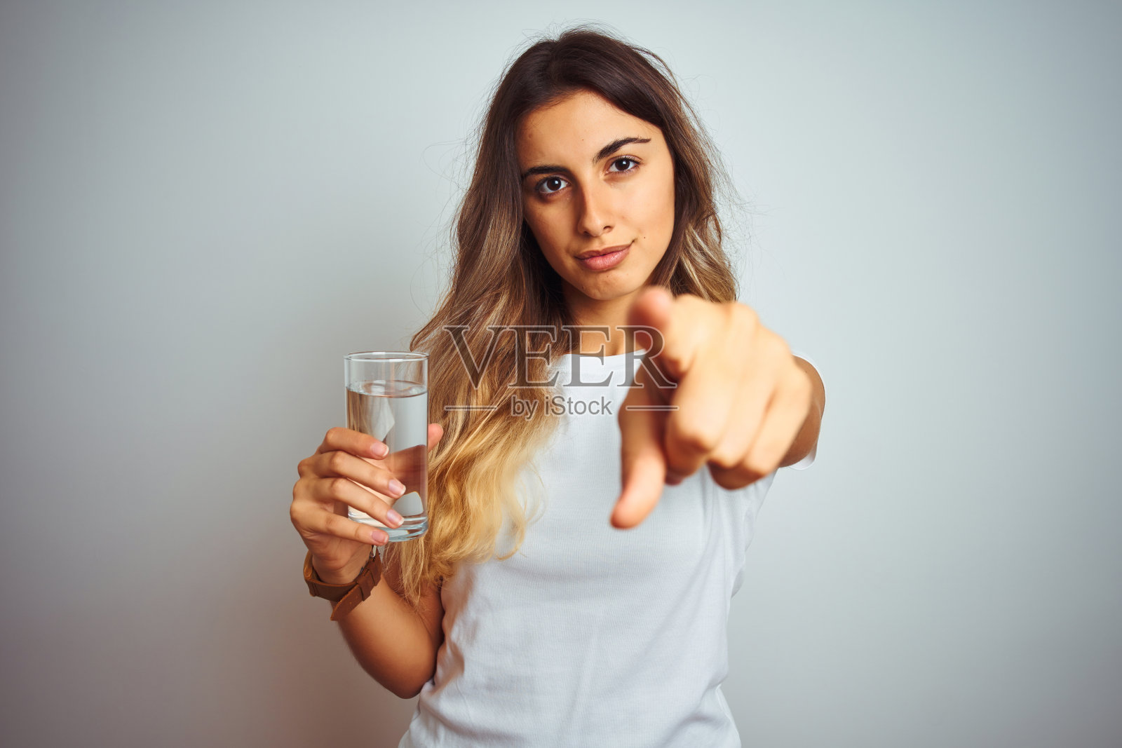 年轻美丽的女人喝一杯水在白色孤立的背景指向相机和你，手势，积极和自信的手势从前面照片摄影图片
