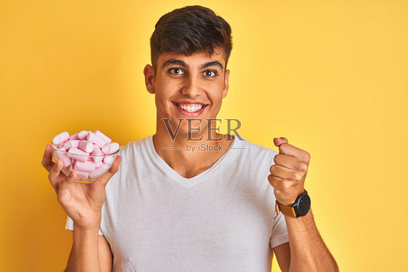 年轻的印度男子拿着碗和棉花糖在孤立的黄色背景尖叫自豪和庆祝胜利和成功非常兴奋，欢呼的情绪照片摄影图片